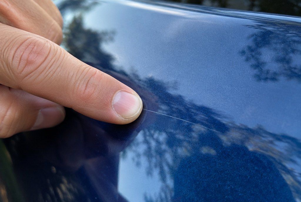 Illustration: a fingernail testing the depth of a fine scratch on blue paint
